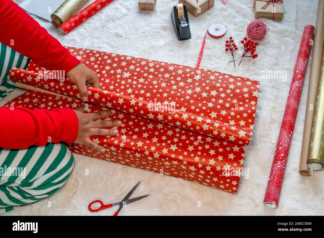 Mani di donna afro-americana che avvolgono i regali di Natale sul tappeto Foto Stock