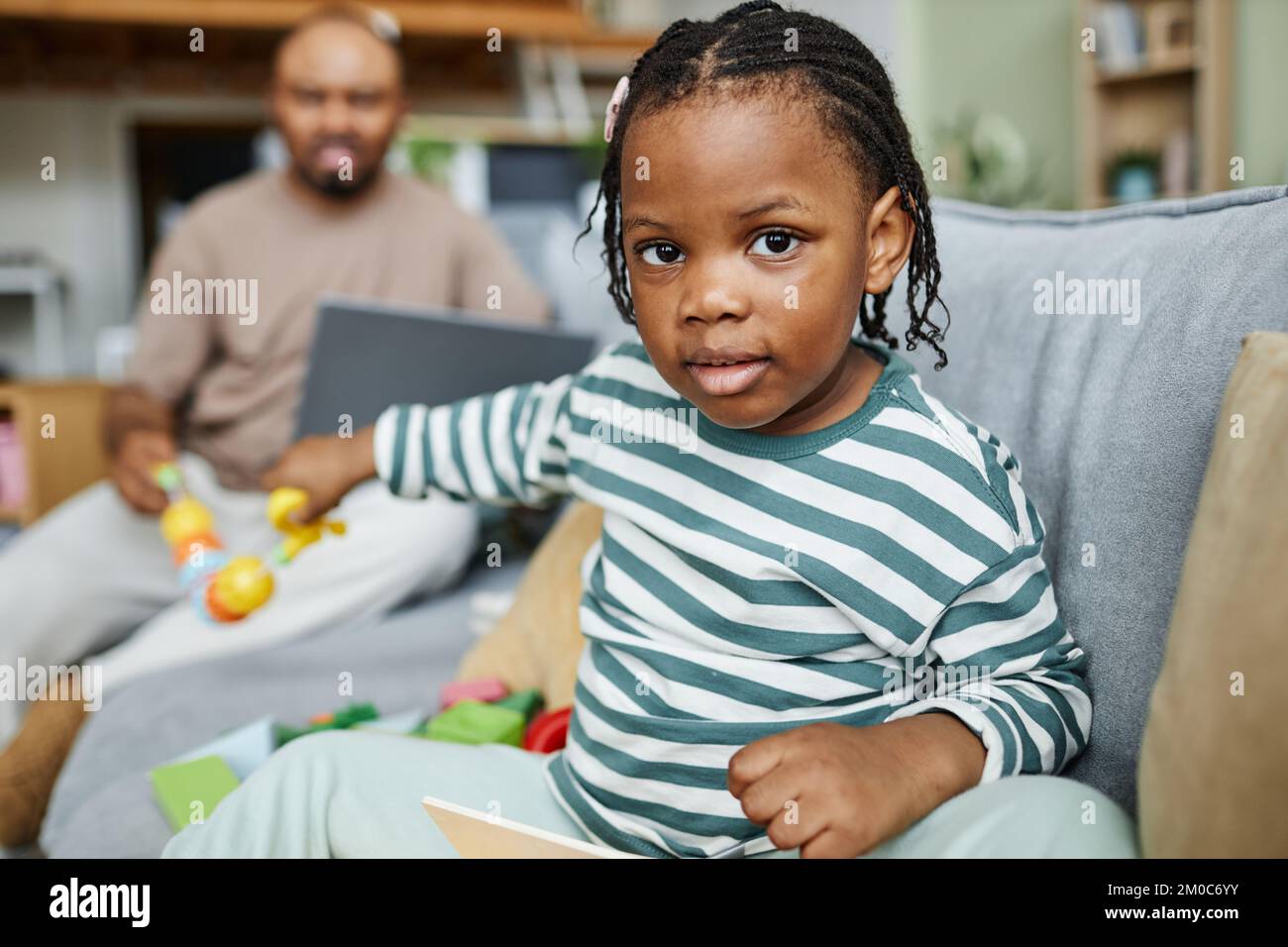 Ritratto di carino bambino nero guardando la fotocamera mentre si gioca sul divano a casa con il padre in background, copia spazio Foto Stock