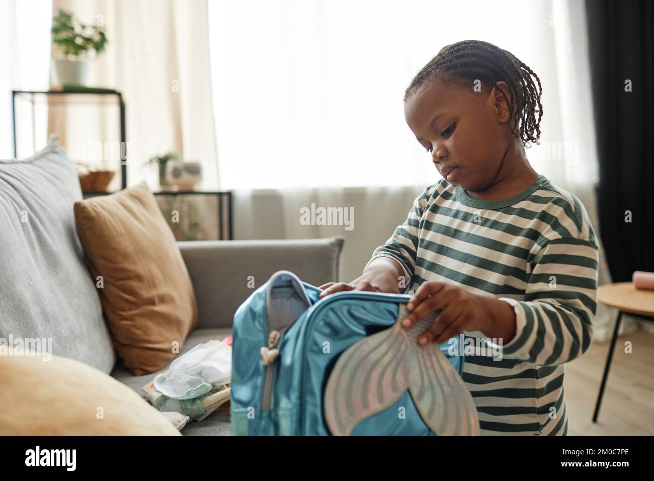 Ritratto di carino bambino nero giocare con la borsa giocattolo in accogliente casa impostazione imballaggio per la scuola materna, copia spazio Foto Stock