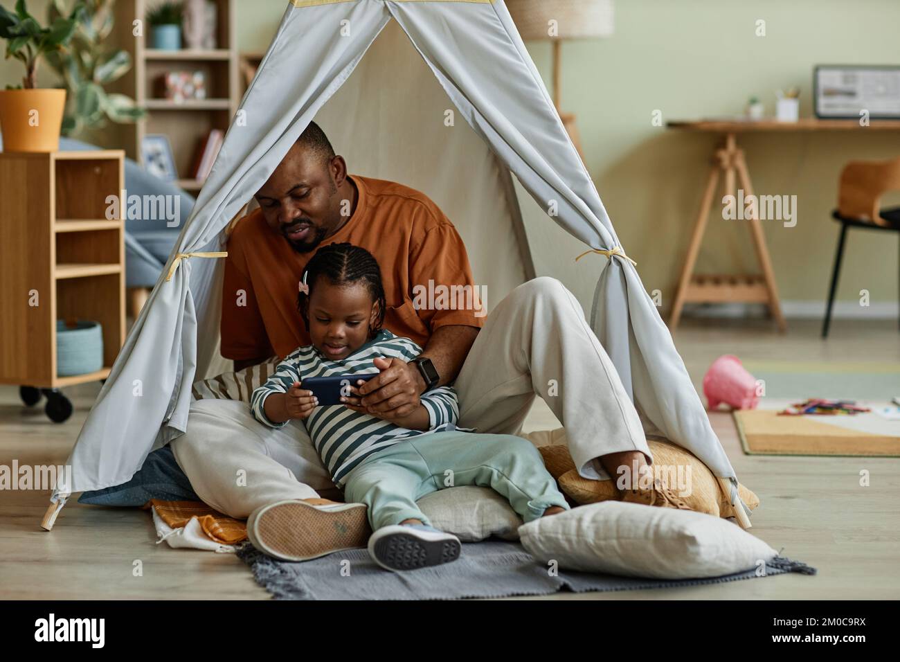 Ritratto completo di amorevole padre nero con bambino utilizzando smartphone insieme in tenda da gioco Foto Stock