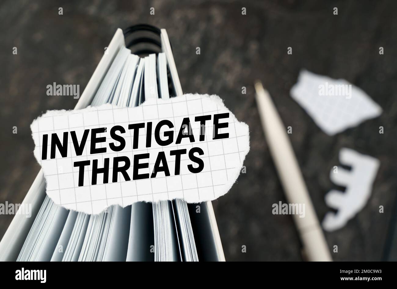 Sul tavolo c'è un notebook su cui si trova un pezzo di carta strappata con l'iscrizione - indagare le minacce. La penna si trova al di fuori della zona di nitidezza. Foto Stock