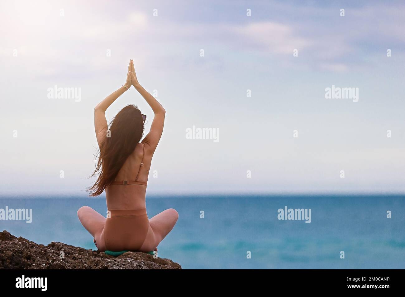 Giovane donna con lunghi capelli che pratica yoga sulla spiaggia Foto Stock