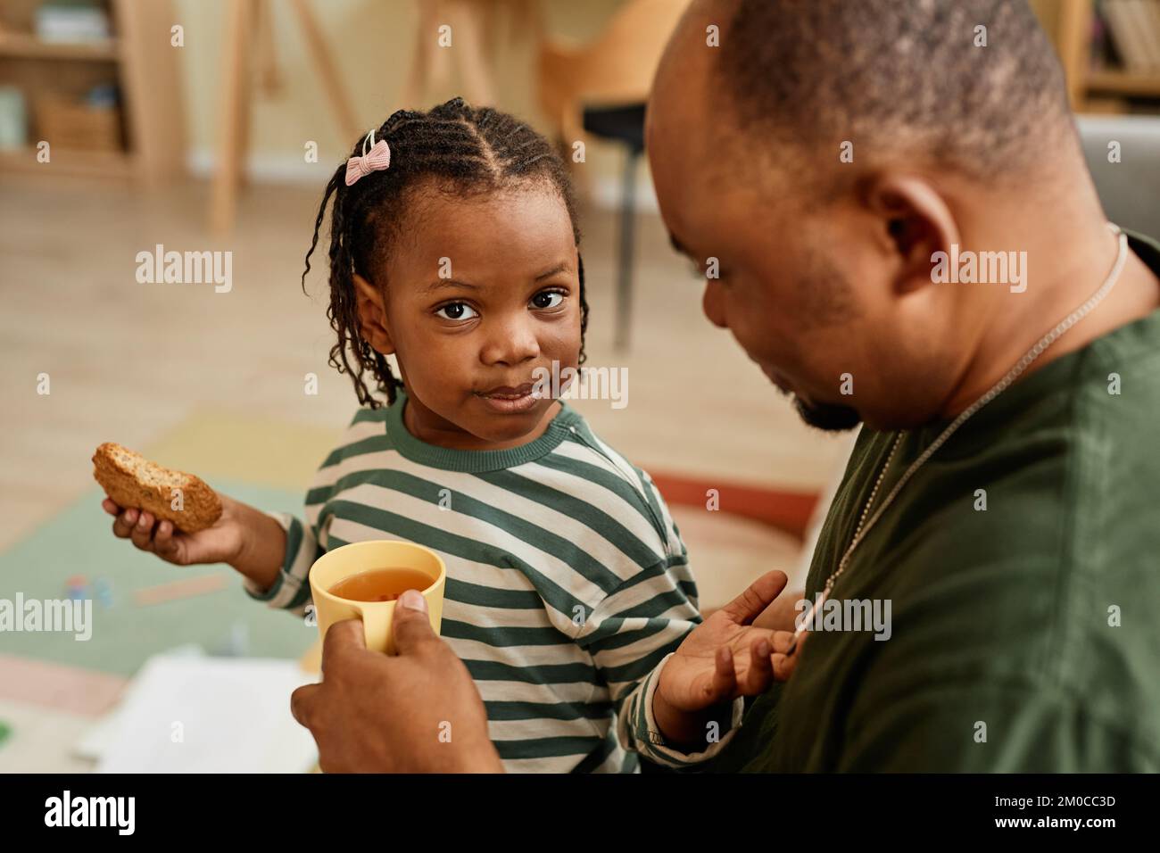 Ritratto ad angolo alto di carina ragazza nera che condivide cookie con il padre e guardando la fotocamera Foto Stock