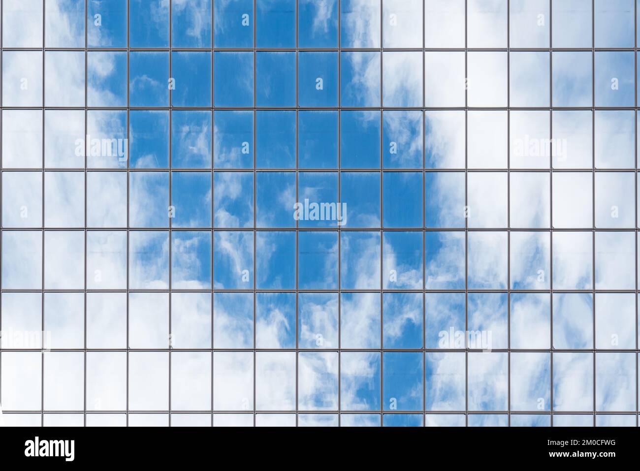 Le nuvole e il cielo blu si riflettono su un alto grattacielo in vetro a specchio Foto Stock