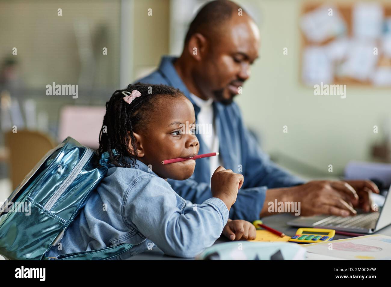 Vista laterale ritratto di bella ragazza nera che gioca con matite mentre il padre lavora in background Foto Stock
