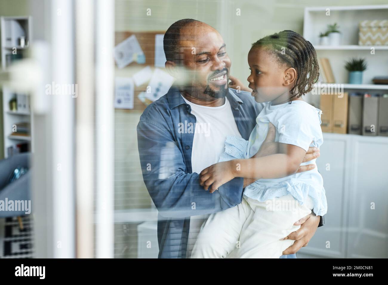 Vita in su ritratto di felice padre abbracciare figlia carina in ufficio dietro parete di vetro, portare il bambino al giorno di lavoro Foto Stock