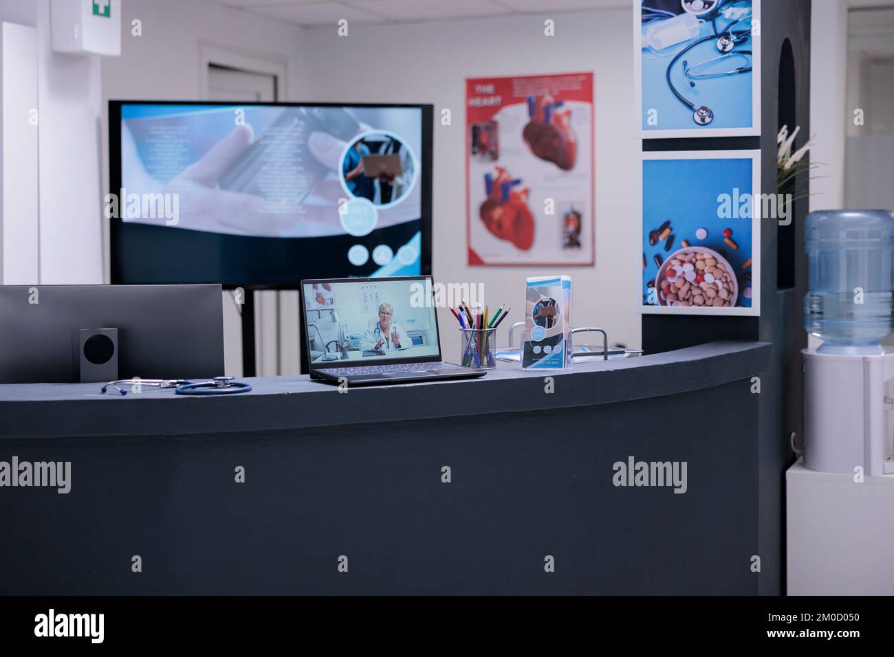 Reception dell'area di ricevimento della clinica medica con poster informativi, forniture per ufficio e computer. Computer portatile sul bancone dell'area di attesa dell'ospedale che mostra il medico generico femminile. Foto Stock