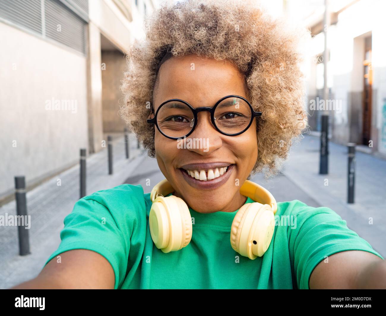 Selfie prospettiva di una felice donna afro-americana con capelli afro indossando occhiali e cuffie in città Foto Stock