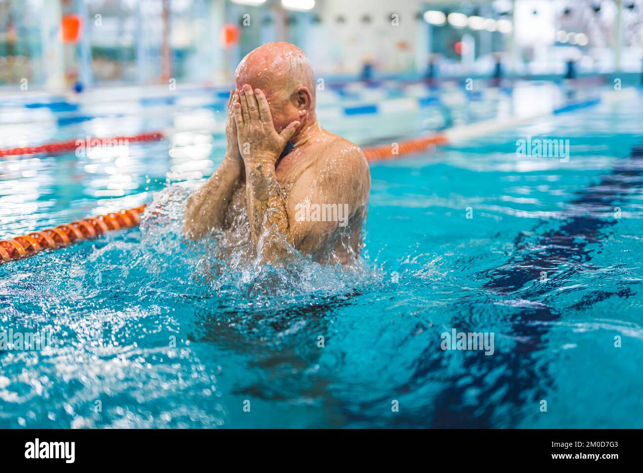 Uomo adulta calvo caucasico irriconoscibile in una piscina che copre il suo volto con entrambe le mani. Attività per il tempo libero. Anziani attivi. Foto di alta qualità Foto Stock