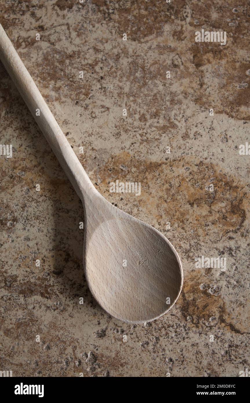 Un cucchiaio di legno su uno sfondo di mattonelle testurizzate in tonalità di marrone. Foto Stock