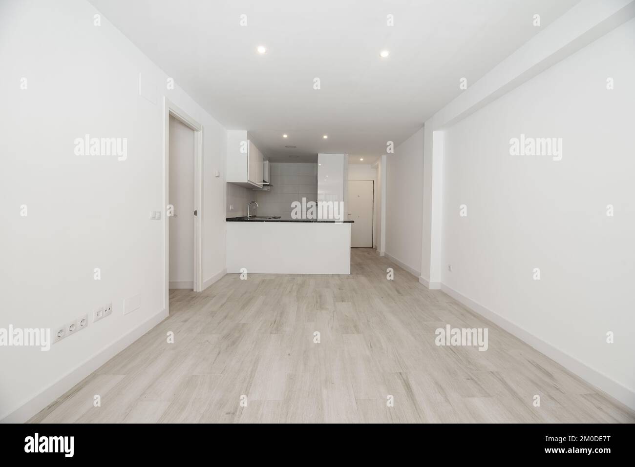 Soggiorno vuoto di una casa con pavimento in laminato di colore chiaro, isola bianca cucina e piano di lavoro nero e faretti integrati nel cei intonaco Foto Stock