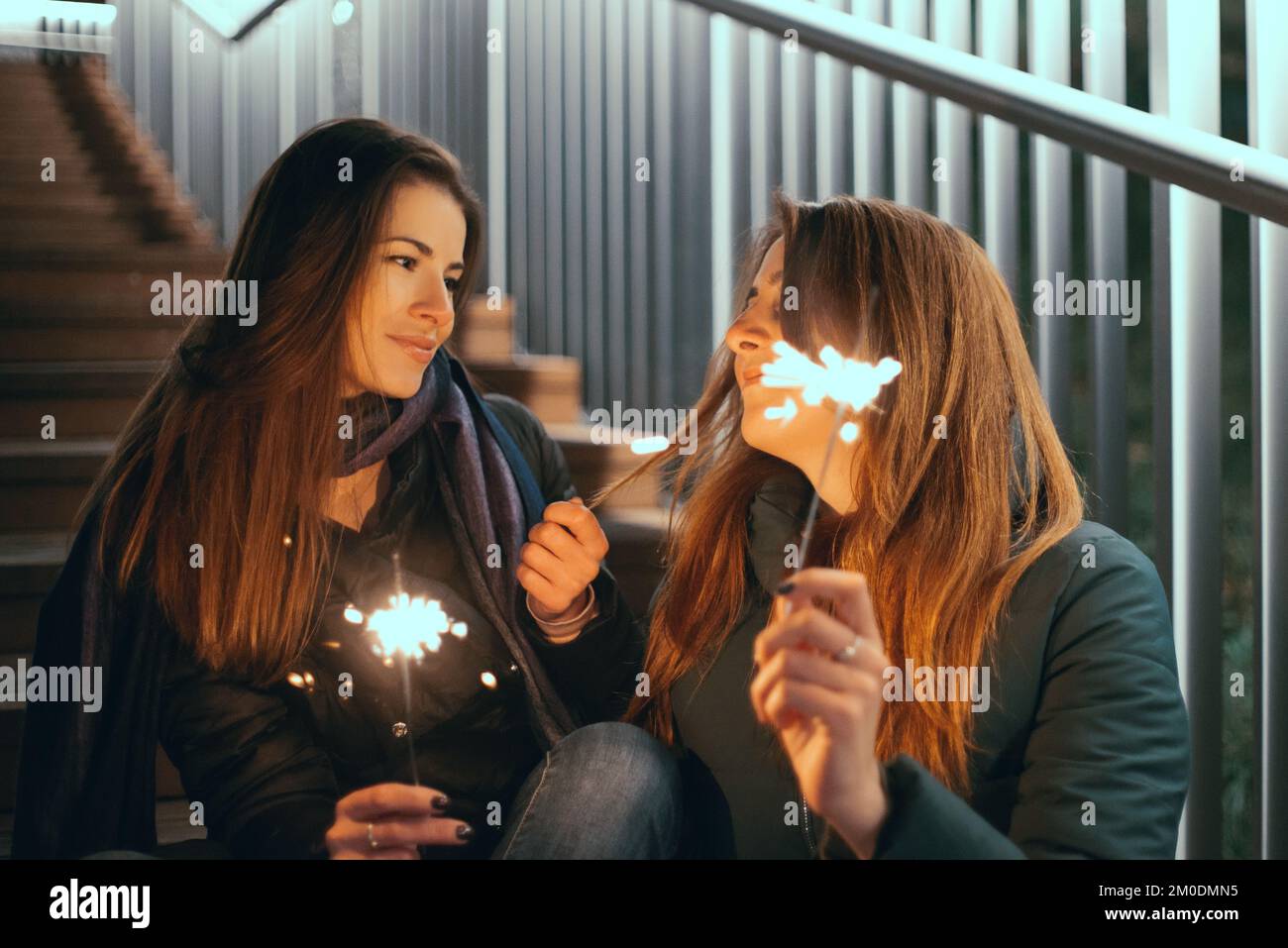 Felice due giovani donne che tengono in mano uno sparkler durante la notte all'aperto a Natale e Capodanno Foto Stock