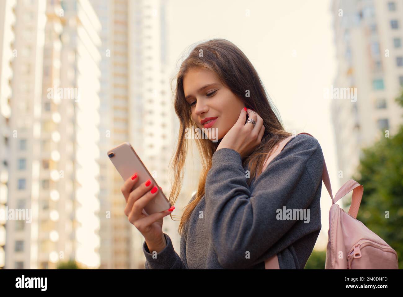 Donna casual sorridente con zaino che utilizza il telefono cellulare iPhone in piedi per strada in centro all'aperto Foto Stock