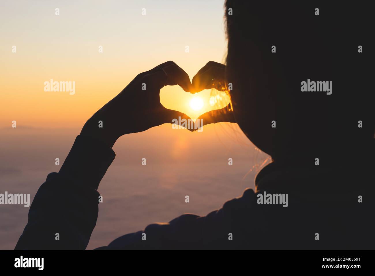 Silhouette. Donna che forma un cuore durante l'alba. Dio è concetto di amore. Forma del cuore. Turismo in montagna. Mostrare amore Amore e sentimenti, dedizione Foto Stock