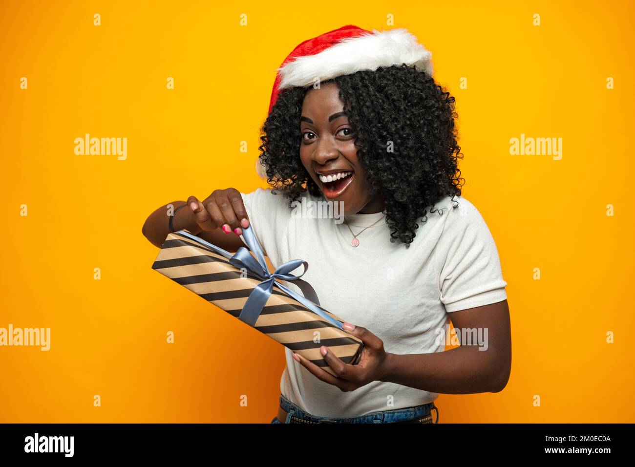 Bella ragazza africana con regalo di Natale in piedi su sfondo giallo Foto Stock
