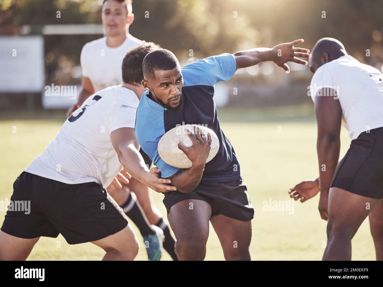 Giocatore di rugby afroamericano che corre via da un avversario mentre tenta di segnare una prova durante una partita di rugby all'esterno su un campo. Uomo nero che fa Foto Stock