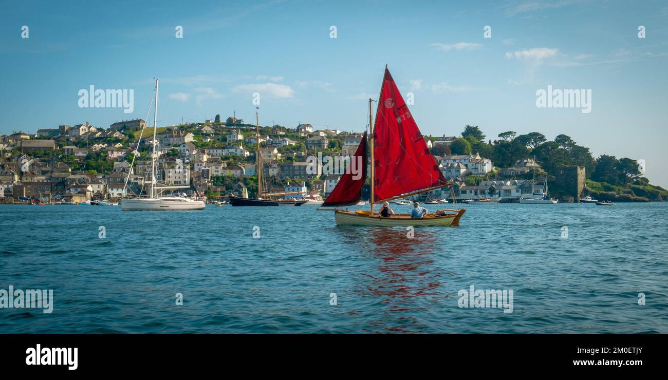 22nd luglio 2021 - Fowey, Regno Unito: La vista da una gita in barca intorno al porto di Fowey, Cornovaglia e la sorprendente vela rossa su una piccola barca di passaggio. Guardando verso Polruan. Foto Stock