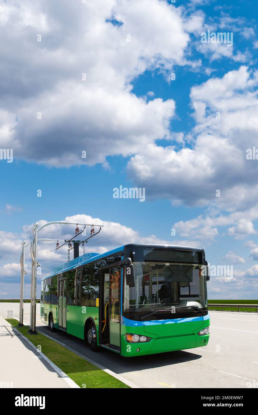 Autobus cittadino elettrico con stazione di ricarica sullo sfondo del paesaggio urbano. Trasporto ecologico e mobilità pulita Foto Stock