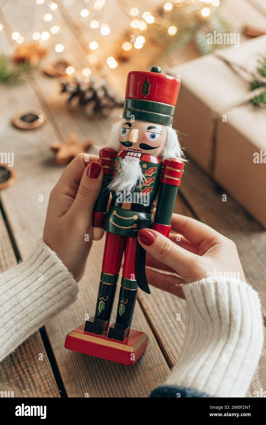 Foto ravvicinata di una donna che tiene un soldato nutcracker in legno di fronte alle luci bokeh e al regalo di natale Foto Stock