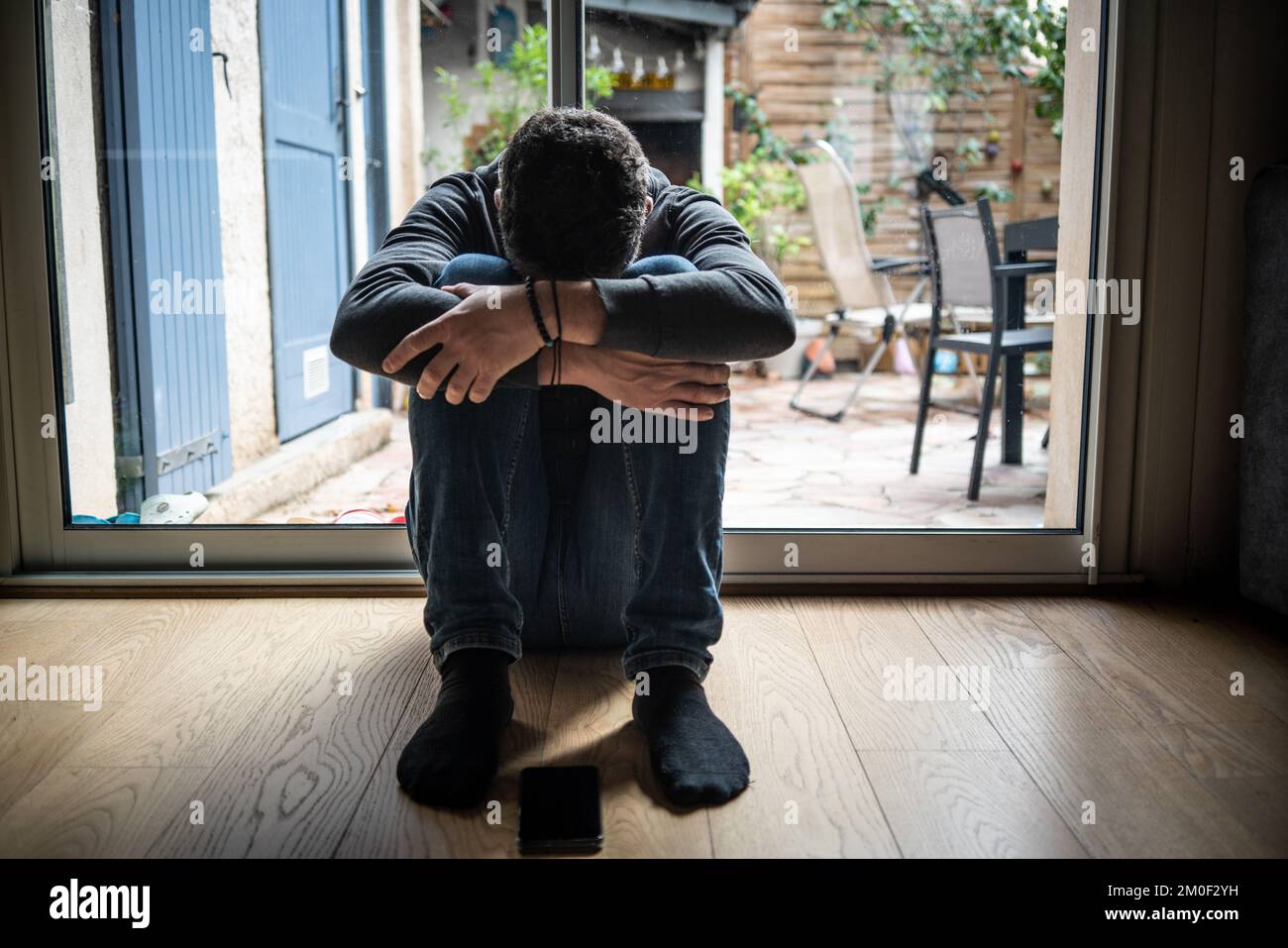 Uomo depresso. Triste uomo infelice seduto sul pavimento e tenendo la testa tra le gambe Foto Stock