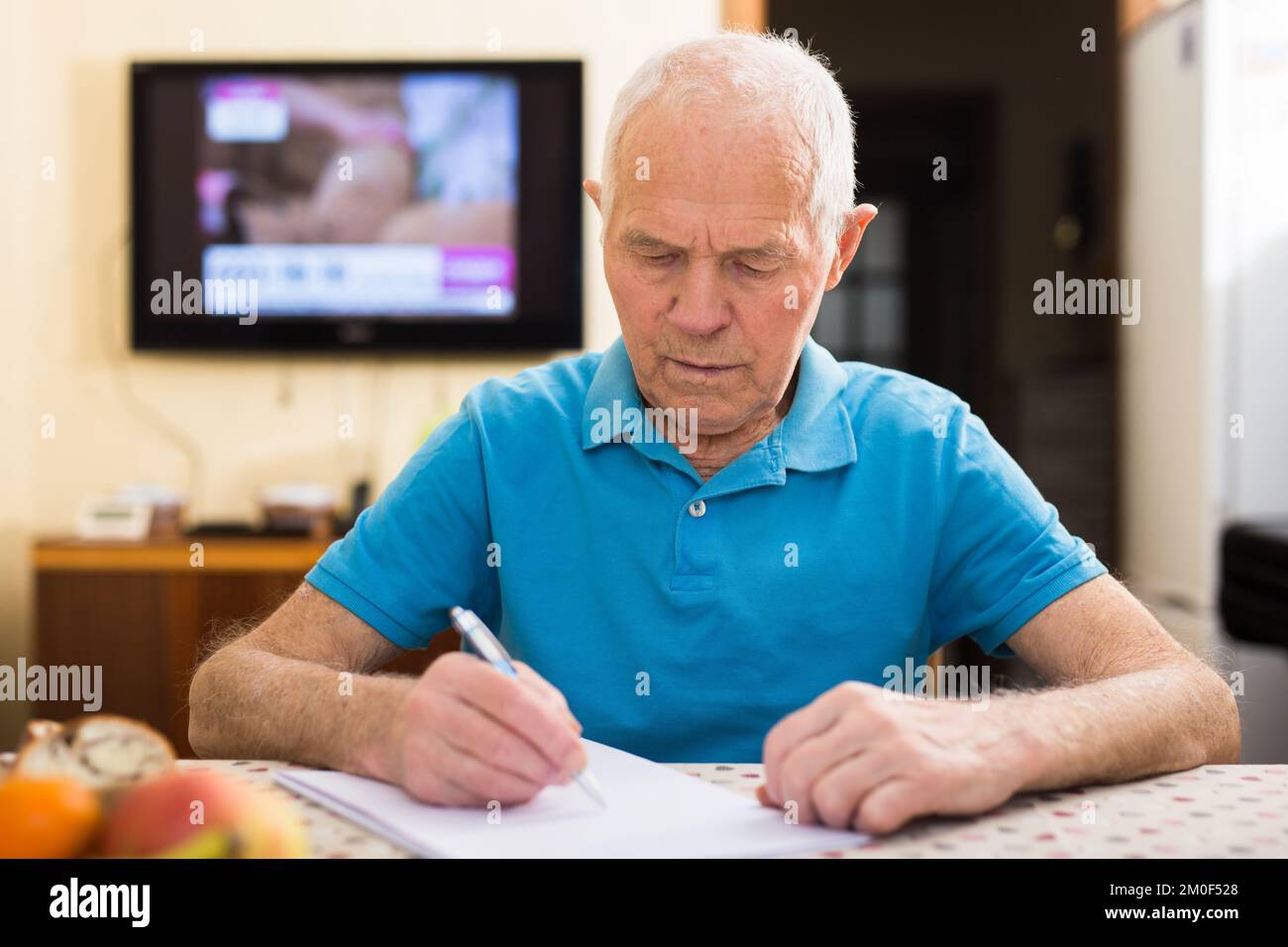Serio uomo anziano scrivere lettera a tavola in soggiorno Foto Stock