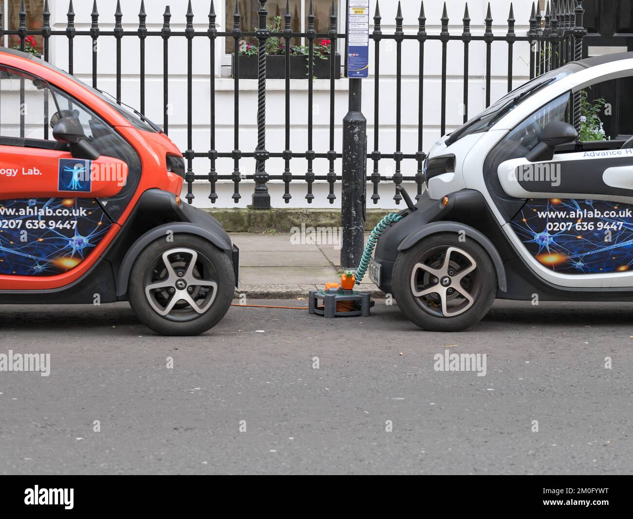 Due auto elettriche intelligenti Renault Twizys che si caricano con una prolunga elettrica collegata a una casa in una strada a Londra, carica EV, EV manuale Foto Stock