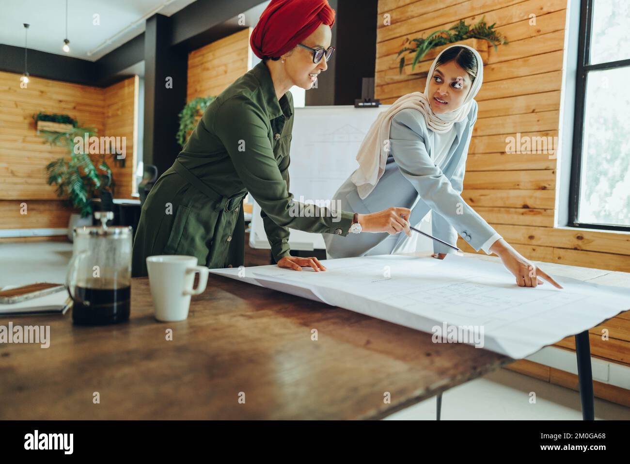 Progettisti musulmani innovativi che hanno una discussione mentre lavorano con disegni BluePrint. Due imprenditrici creative che progettano un nuovo progetto. Archi femmina Foto Stock