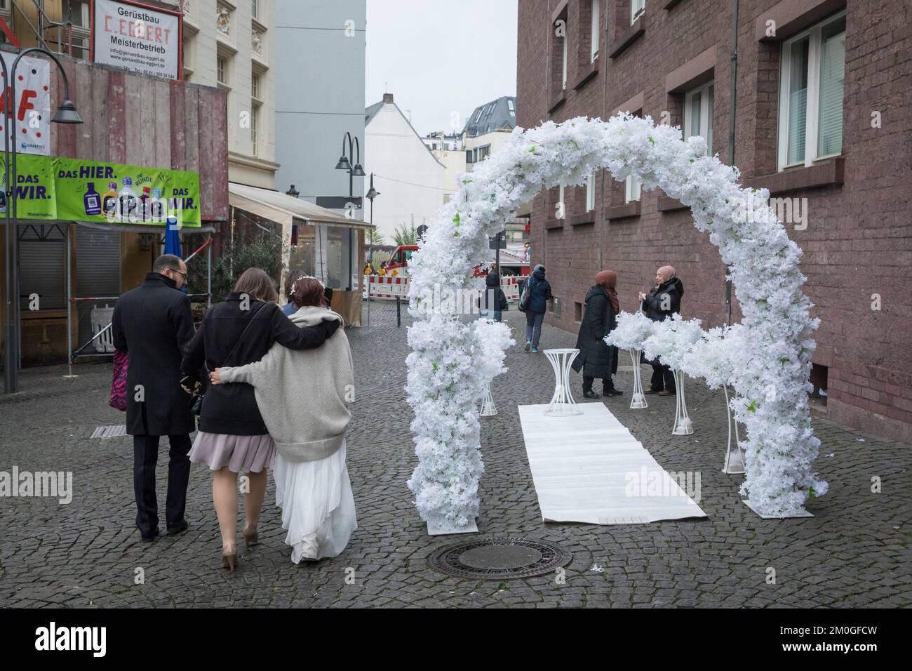 Una sposa viene con le scorte dall'ufficio di registro nella città vecchia e passa un arco di nozze, Colonia, Germania. Eine Braut kommt mit Begleitern vom S Foto Stock