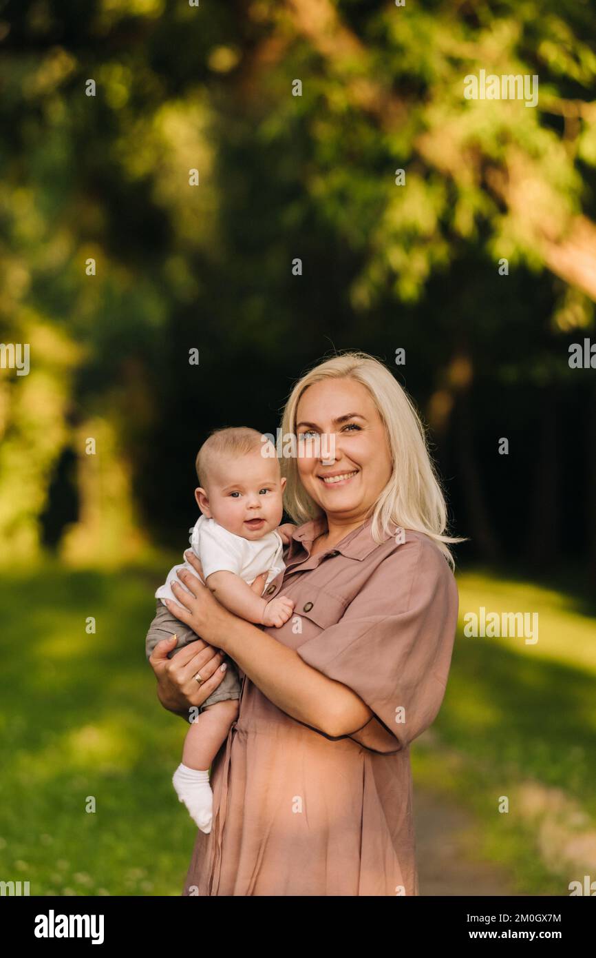Una madre tiene in braccio un bambino felice in un parco estivo Foto Stock