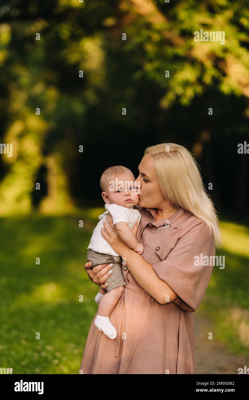 Una madre tiene in braccio un bambino felice in un parco estivo Foto Stock