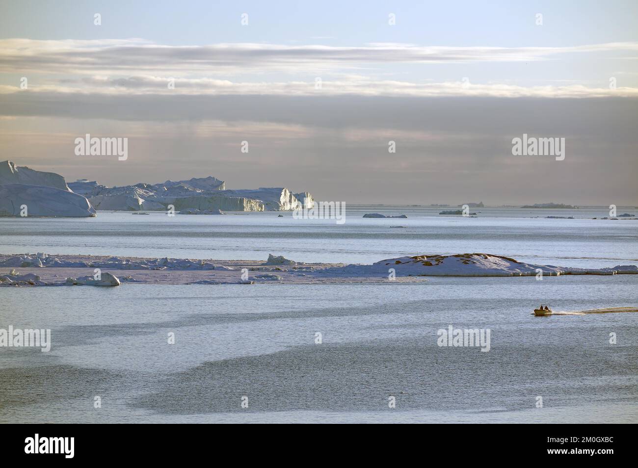 Piccola barca di fronte alle rocce, ghiaccio e iceberg enormi, luce soffusa sera, Baia di Disko, Ilulissat, Groenlandia, Danimarca, Nord America Foto Stock