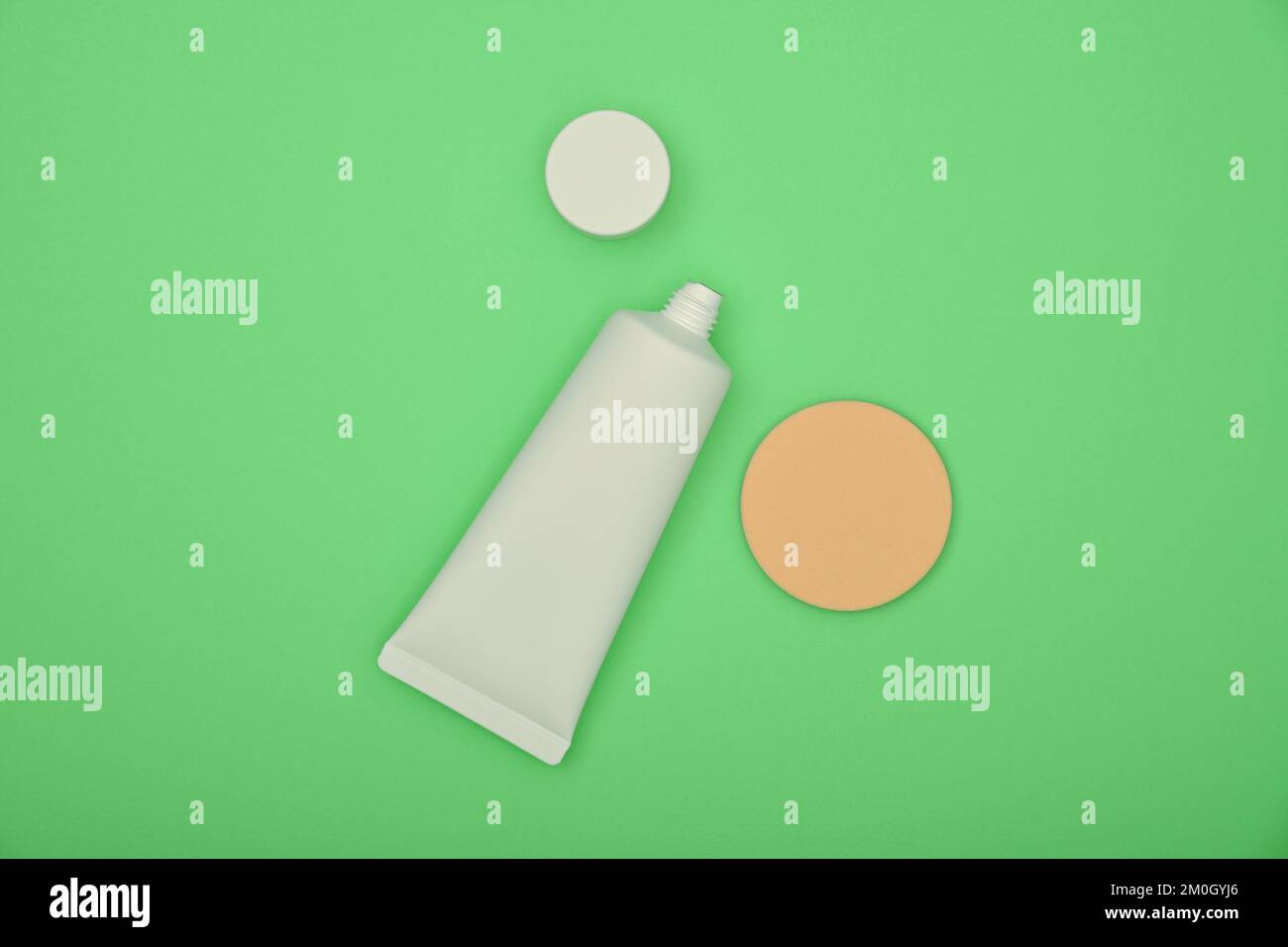 Chiudere un tubo bianco di crema di base per il trucco e spugna beige su sfondo verde naturale, vista dall'alto rialzata, direttamente sopra Foto Stock