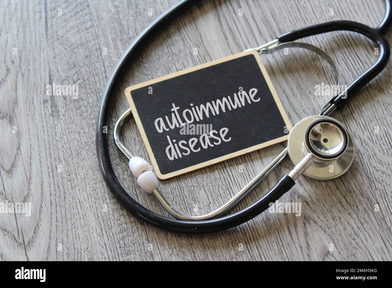 Stetoscopio e lavagna con testo MALATTIA AUTOIMMUNE su tavolo di legno. Concetto medico e sanitario Foto Stock