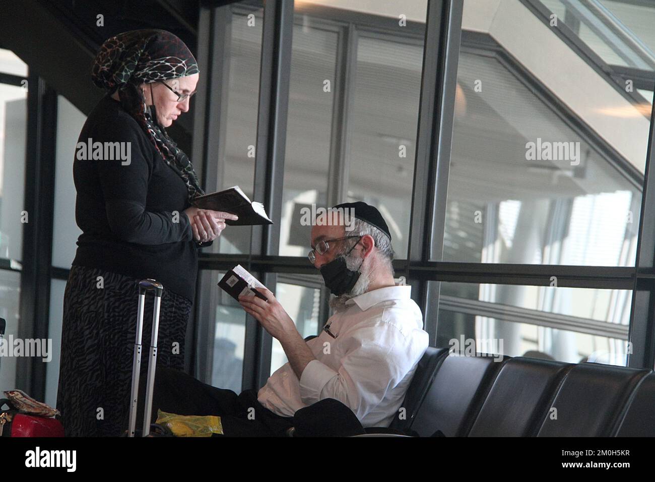 Una coppia ebraica che legge mentre scrive nel terminal di un aeroporto internazionale Foto Stock