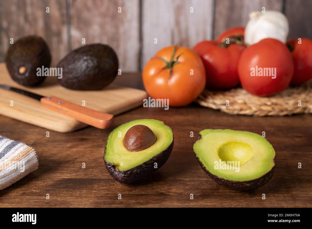 Avocado tagliato in due, con fondo in legno con pomodori, aglio e altri avocado. Foto Stock