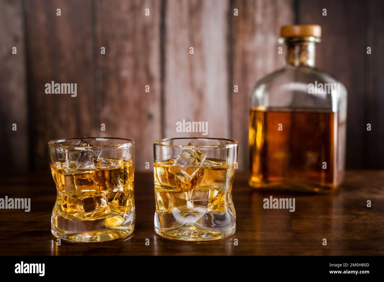 Due bicchieri di whiskey con cubetti di ghiaccio, con una bottiglia con whiskey sullo sfondo fuori fuoco. Foto Stock