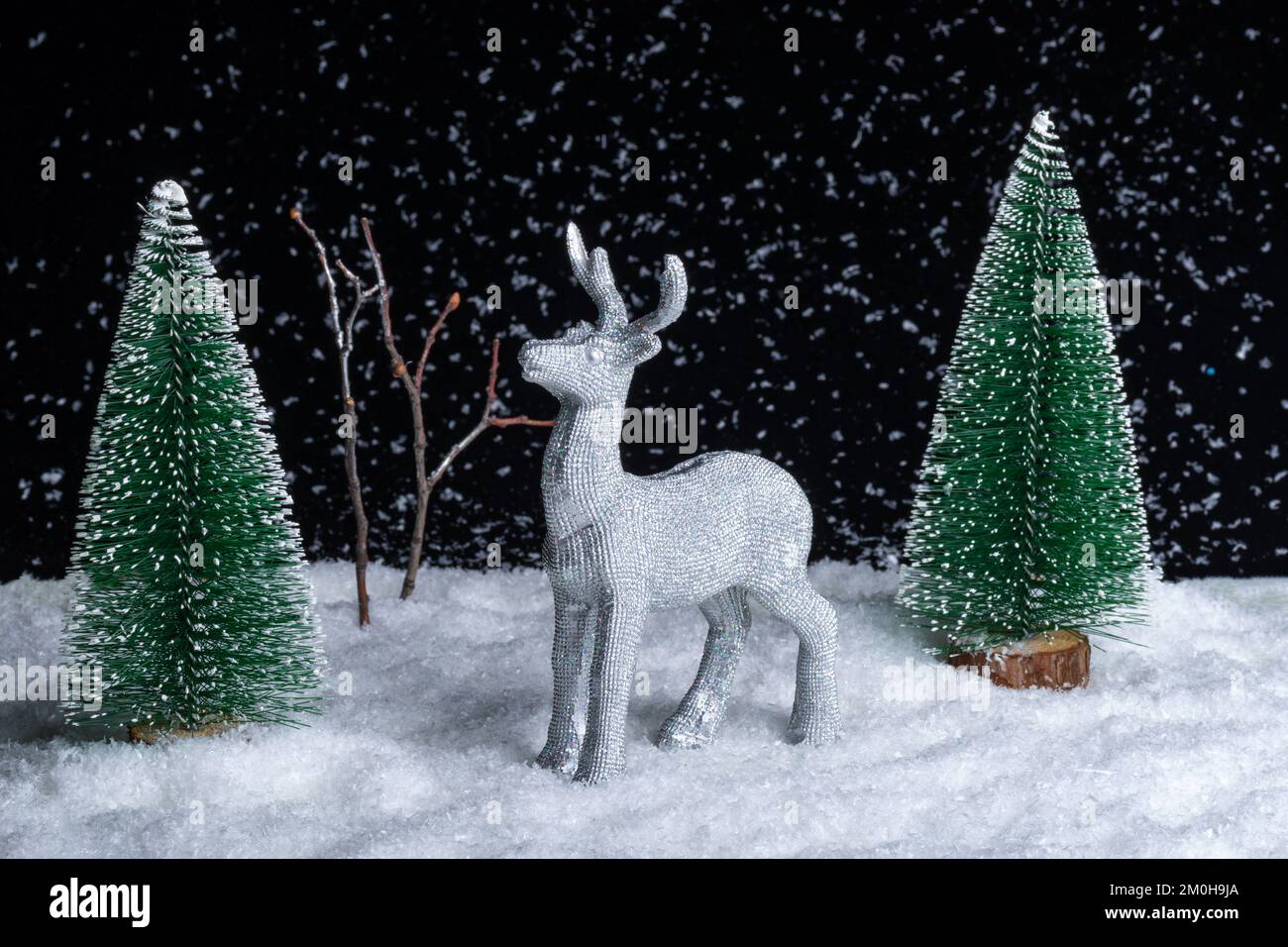 Carta di Natale creativa. Un giocattolo che splende cervi d'argento in piedi nella neve nella foresta tra gli alberi di Natale di notte su uno sfondo nero. Babbo Natale Foto Stock