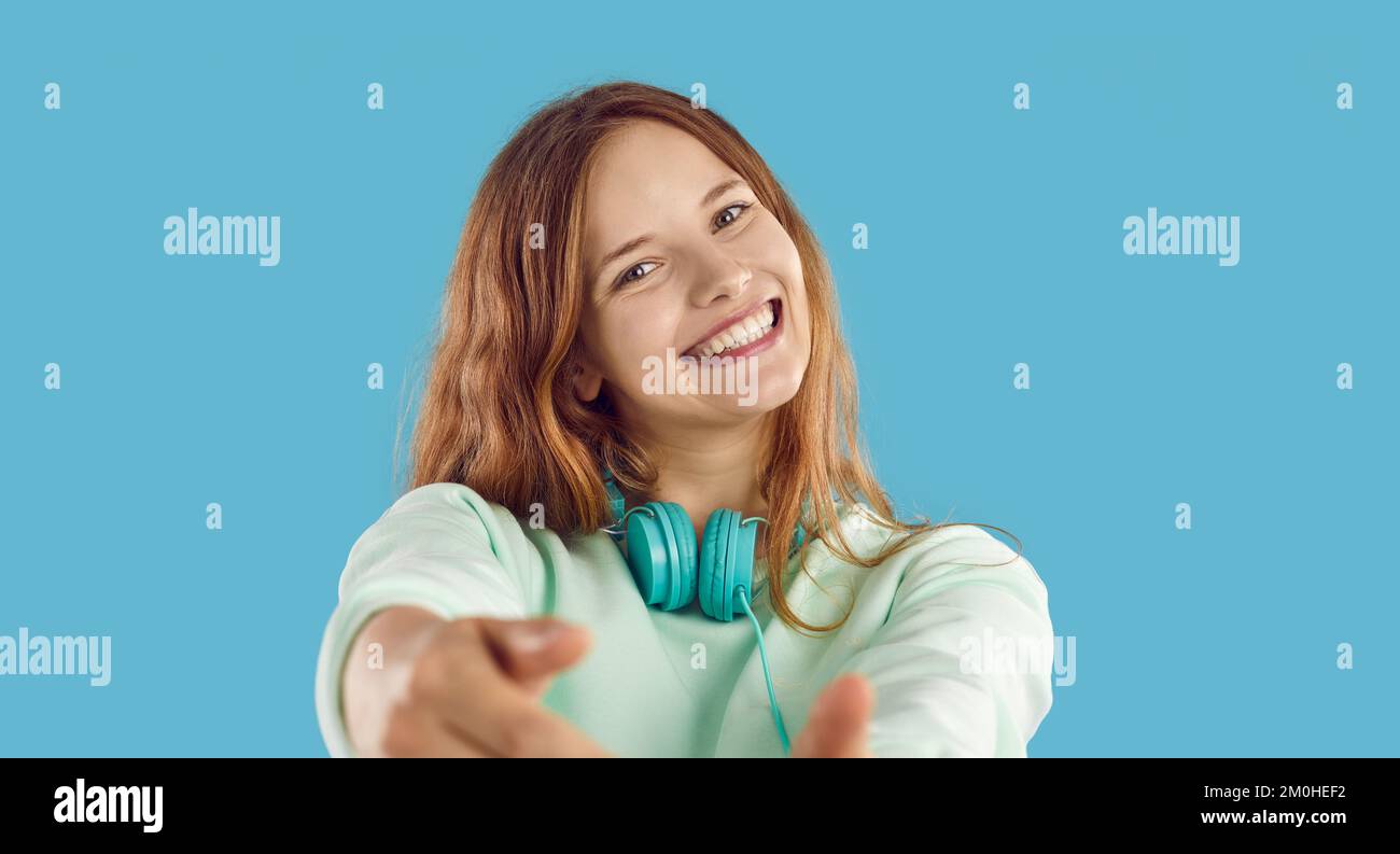 Ragazza felice con le cuffie guardando la fotocamera e sorridendo su sfondo blu studio Foto Stock