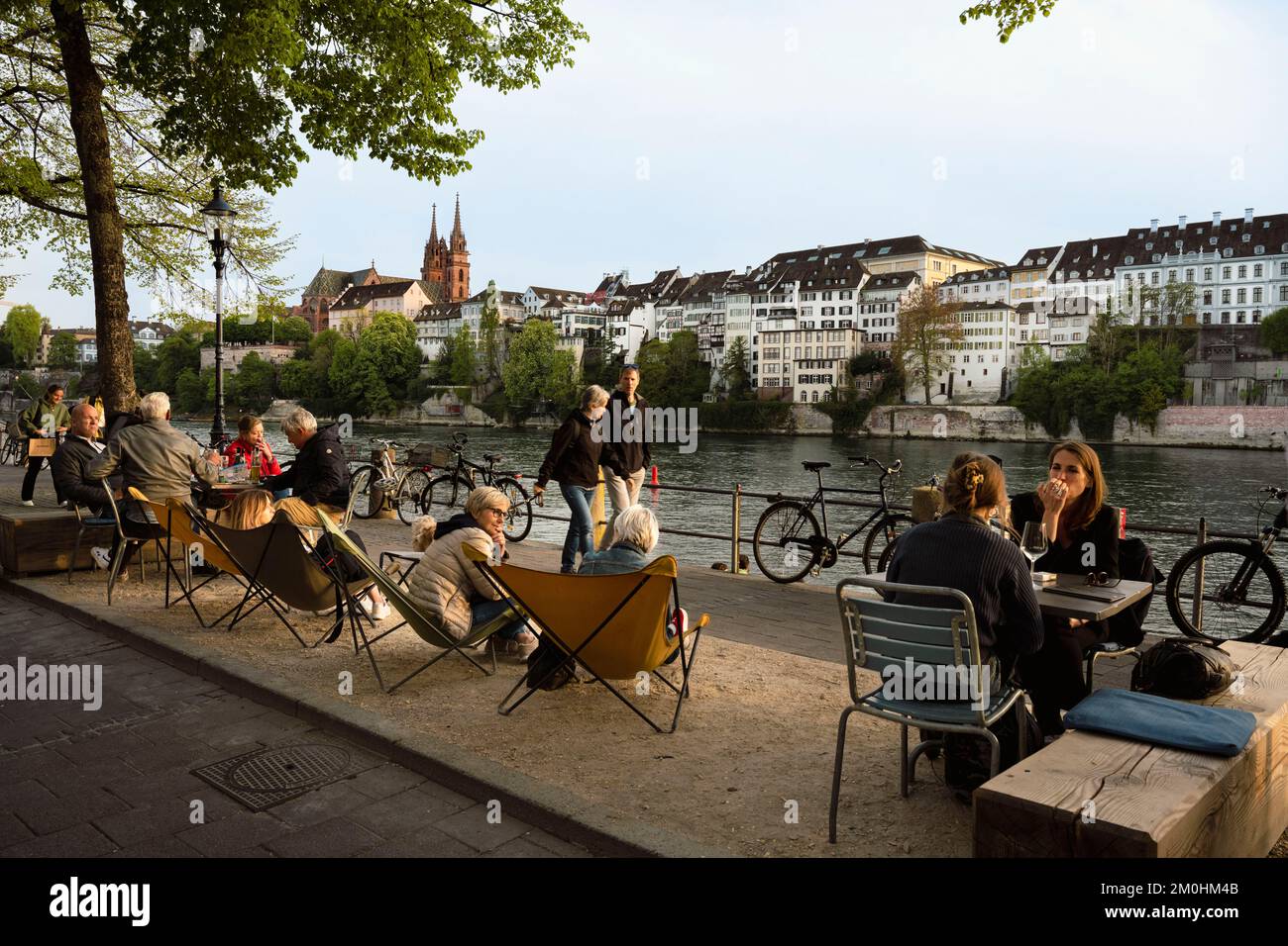 Svizzera, Canton Basilea-Città, Basilea, banchine del distretto di Little Basel sulla riva destra del fiume Reno e il Minster o Cattedrale protestante di nostra Signora di Basilea (Munster) sullo sfondo, ristorante e caffè? le terrazze prendono vita al crepuscolo Foto Stock