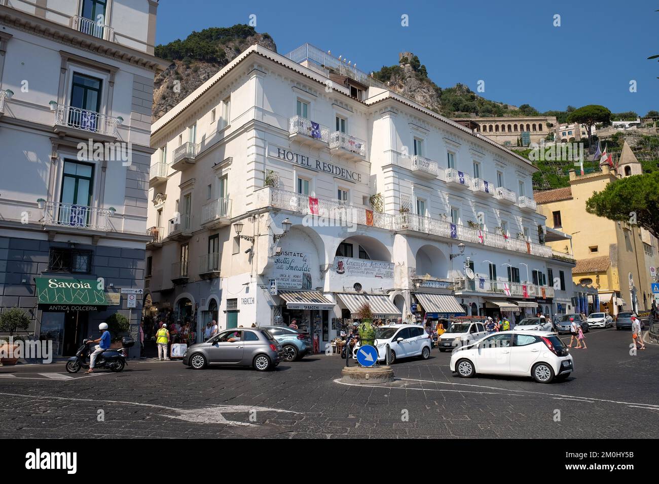 La strada principale che passa per Amalfi vicino al porto mostra le auto che navigano lungo la piccola rotonda con l'Hotel Residence e Savoia sullo sfondo. Foto Stock