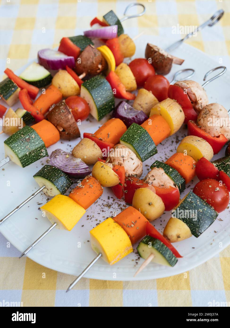 Spiedini con verdure miste (zucchine, patate, carote, peperone, funghi) su un piatto, pronti per essere grigliati. Foto Stock