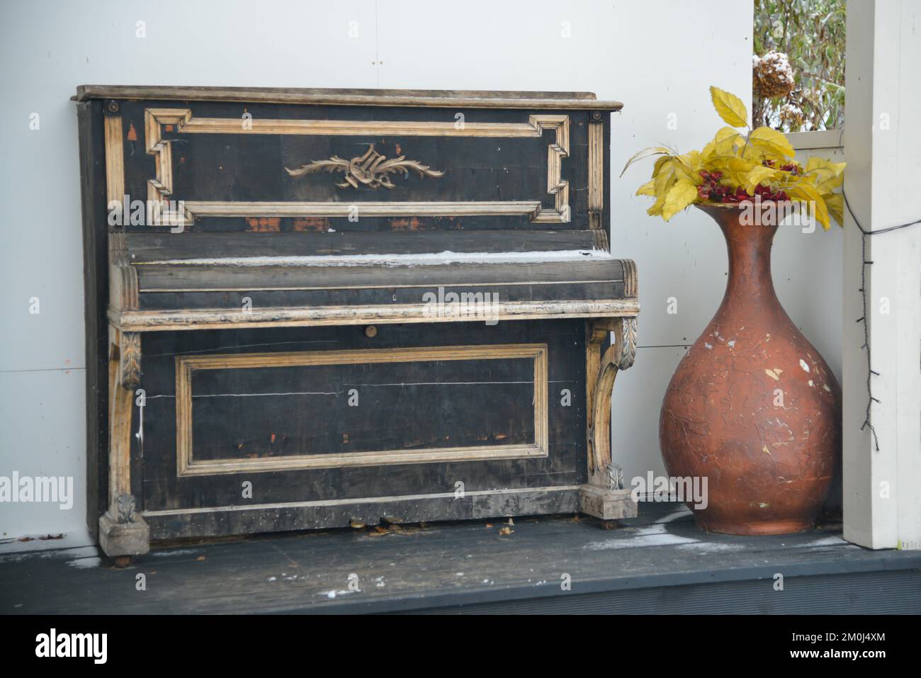 Vecchio piano retrò d'epoca accanto a un vaso di fiori di argilla marrone sulla parete di una casa di legno bianco. Foto Stock