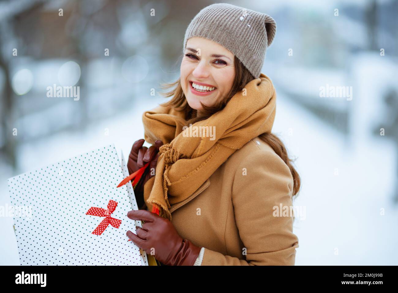 felice donna elegante in cappello marrone e sciarpa in camel cappotto con  borse per la spesa fuori in città in inverno Foto stock - Alamy