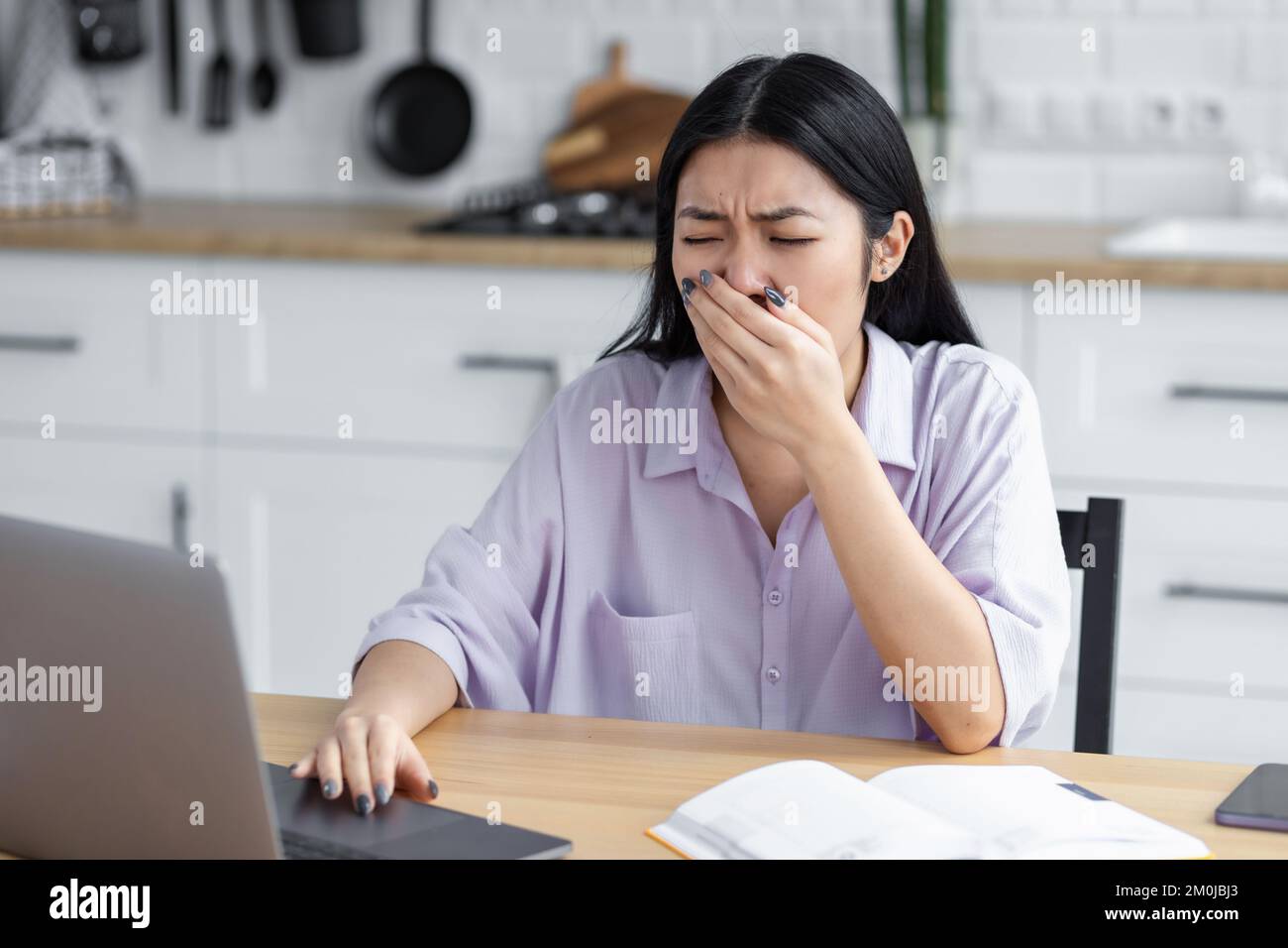 Donna asiatica stanca freelancer o studente sbadigliano copre la bocca seduta sul posto di lavoro a casa Foto Stock