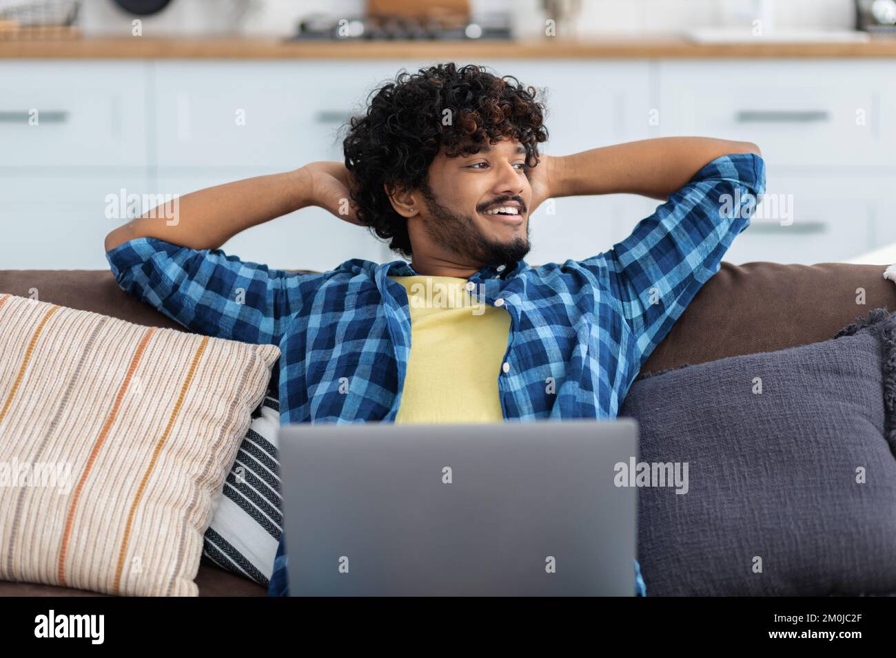 Felice uomo asiatico sorridente freelancer con notebook appoggiato con le mani dietro la testa distratto dal lavoro online Foto Stock