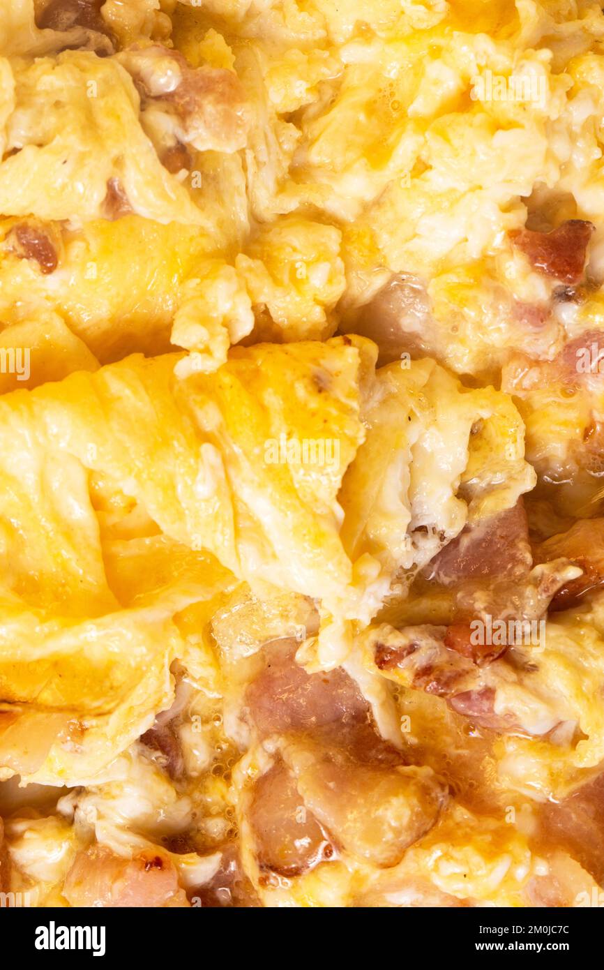 Consistenza di gustose uova strapazzate con pancetta come sfondo, primo piano. Foto macro. Foto Stock