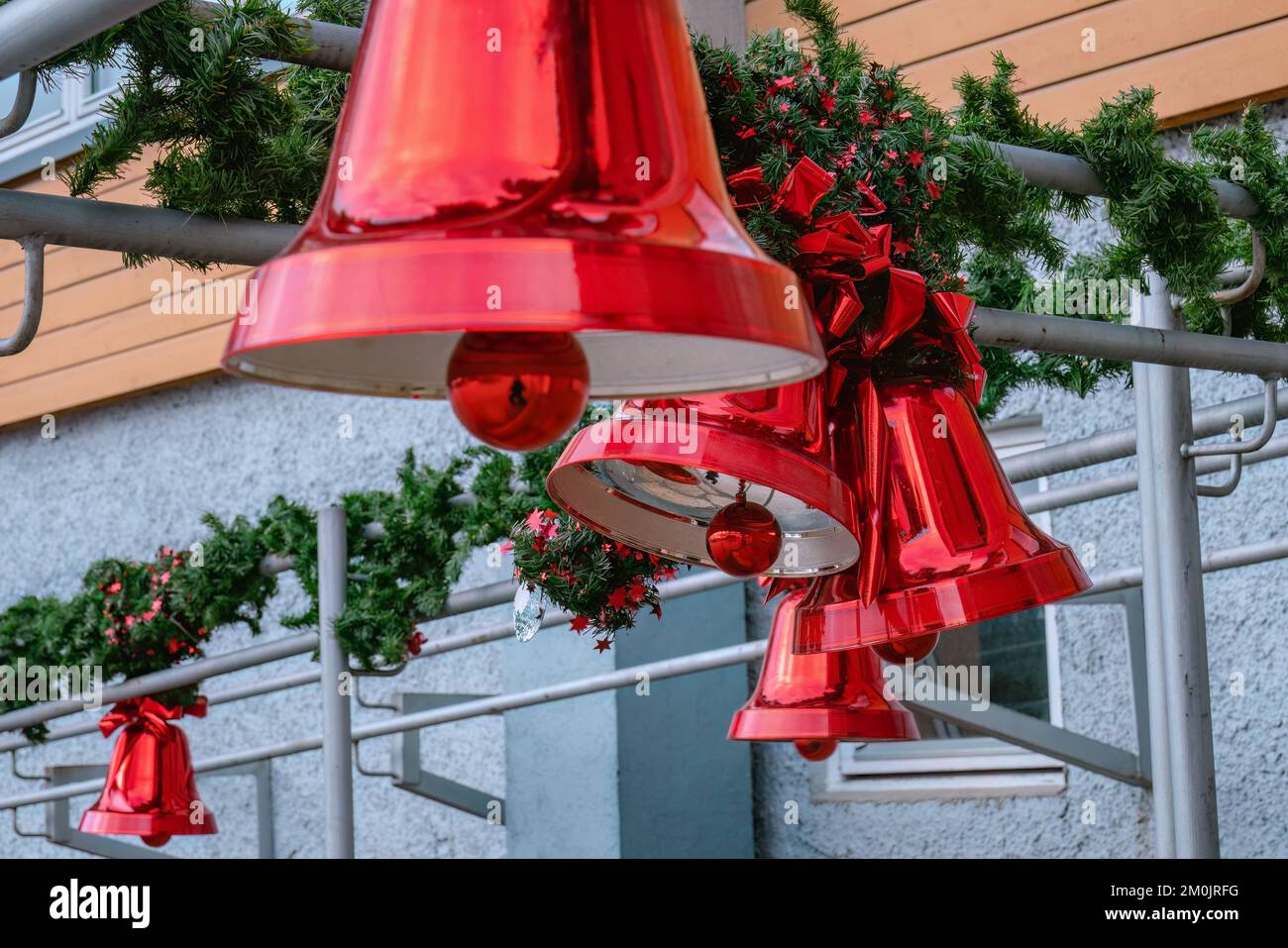 Molte grandi campane rosse di Natale con arco rosso e foglie di pino, decorazione di strada di Natale, fuoco selettivo su campane di sfondo, campana anteriore sfocata Foto Stock