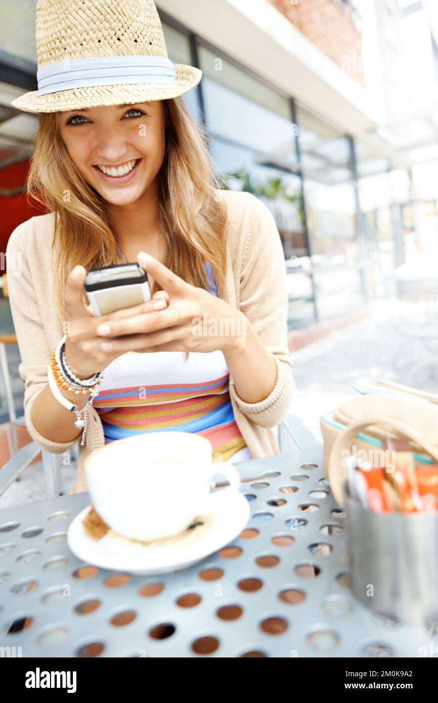 Questo ristorante ha ricevuto una buona recensione. Una giovane donna informale che invia un messaggio di testo mentre si siede in un caffè marciapiede in città - ritratto. Foto Stock