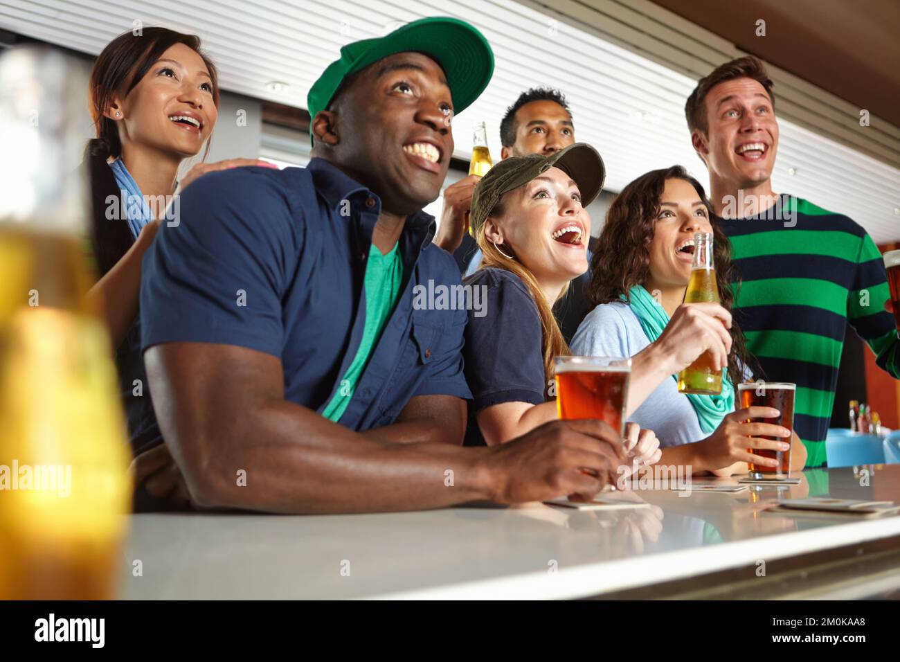 Le bevande alleviano la tensione degli sport di sabato. Un gruppo di amici che allietano la loro squadra di sport preferita al bar. Foto Stock