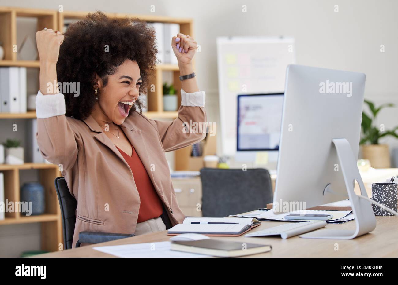 Una donna d'affari afroamericana di razza mista con un afro che esprime gioia mentre festeggia una vittoria al suo lavoro d'ufficio. Donna ispanica cercando di successo Foto Stock